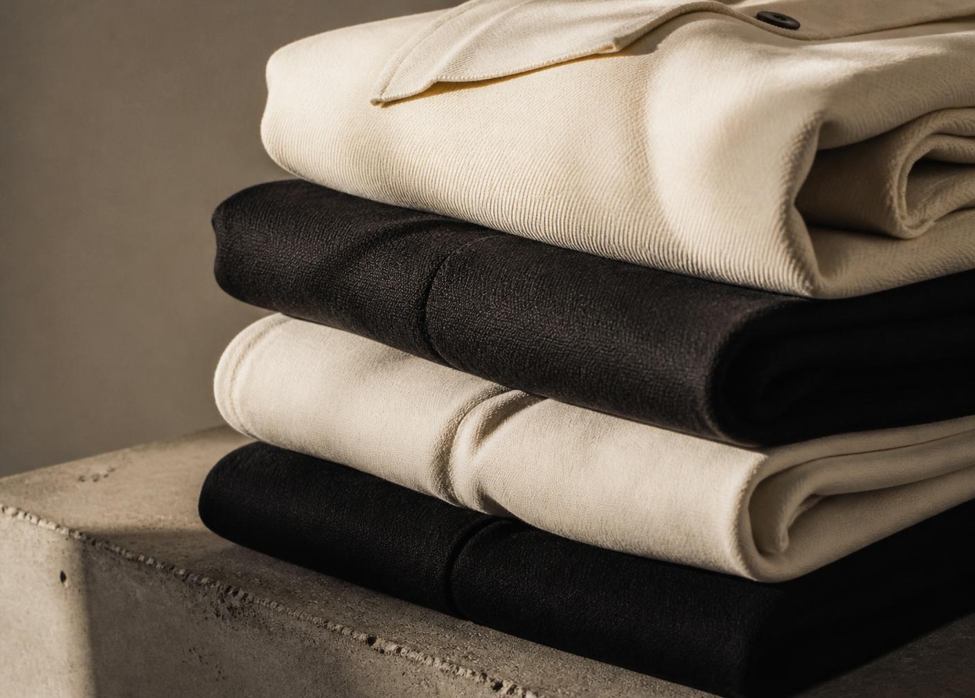 Folded ivory and black garments stacked on a concrete plinth